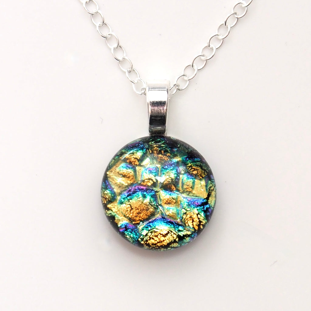 A round pendant necklace featuring an iridescent, mosaic-like pattern with gold, blue, green, and purple hues, suspended from a silver link chain on a plain white background.